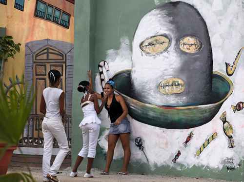 A girl takes a photograph with a mobile phone in a square adorned by murals in Havana